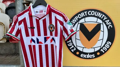 BBC Newport County's away kit for 2025/26, commemorating the Children of '37 - Basque refugees fleeing the Spanish Civil War who were resettled in Caerleon. On the left is the shirt which is a red and white striped football shirt, and on the right is the Newport County logo. It says "Newport County AFC 1921 Exiles 1989".