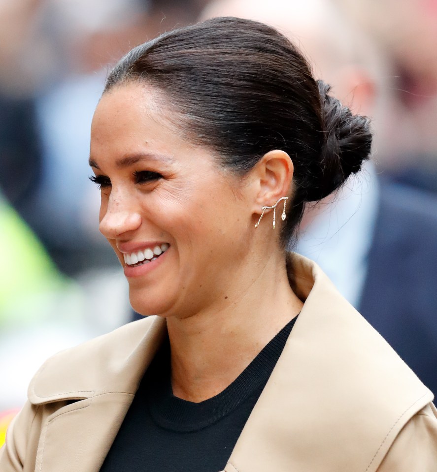 Meghan, Duchess of Sussex, smiling and wearing a beige coat.