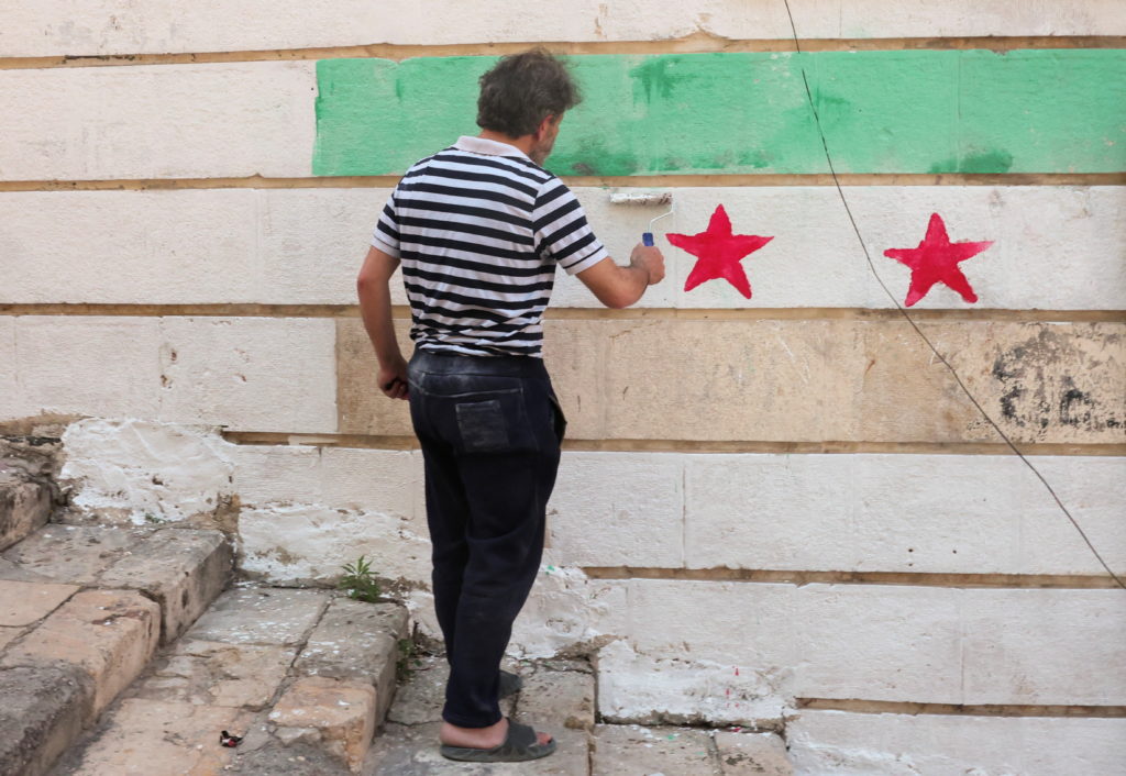 A man paints Syria's flag on a wall as U.S. President Donald Trump announced that he would order the lifting of sanctions ...