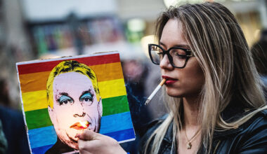 A woman lights a cigarette placed in a rainbow placard depicting Hungary's Prime Minister Viktor Orban
