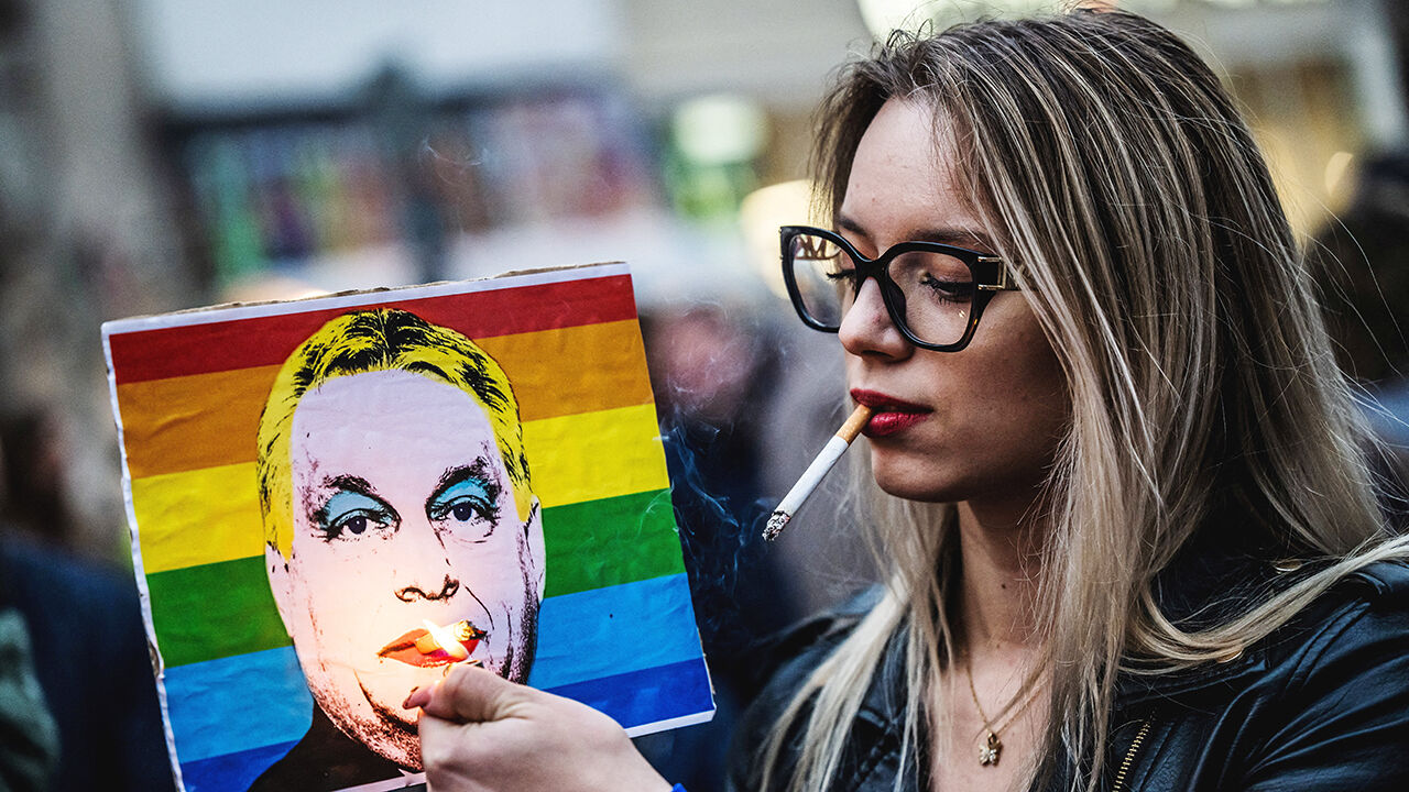 A woman lights a cigarette placed in a rainbow placard depicting Hungary's Prime Minister Viktor Orban
