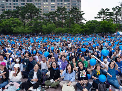 People holding light sticks and blue balloons cheer during a political rally