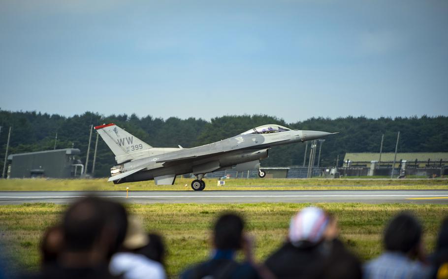 A military F-16 fighter jet lands on a runway at an airfield with spectators watching in the foreground. 