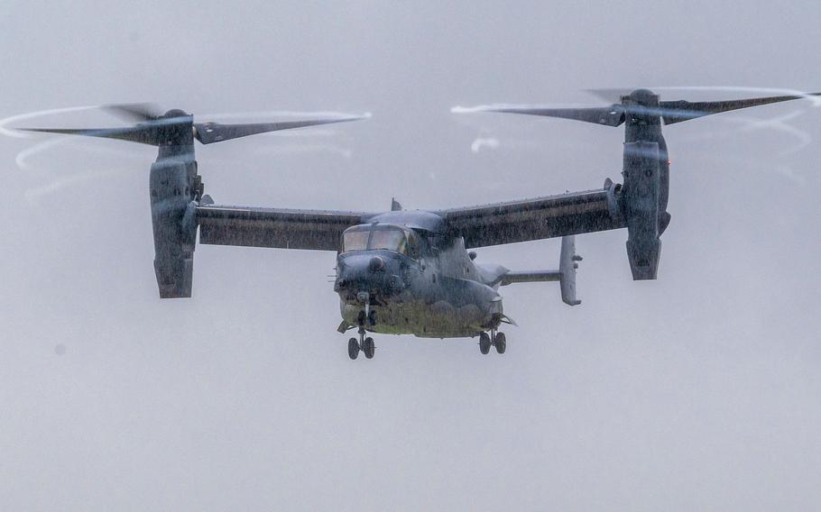 A V-22 Osprey tiltrotor aircraft flies through overcast skies with its twin rotors in horizontal position for forward flight.