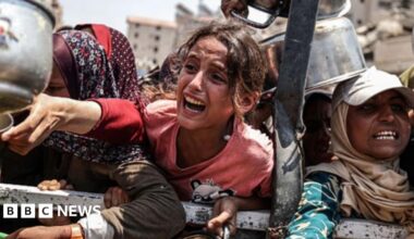 A girl is seen crying as she holds a pot to collect food in a crowd as Palestinians face food shortages in Gaza on 28 July 2025.