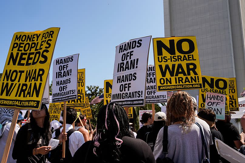 Two anti-war demonstrators hold signs outside the Wilshire Federal Building in Los Angeles following US air strikes on Iran, 22 June, 2025