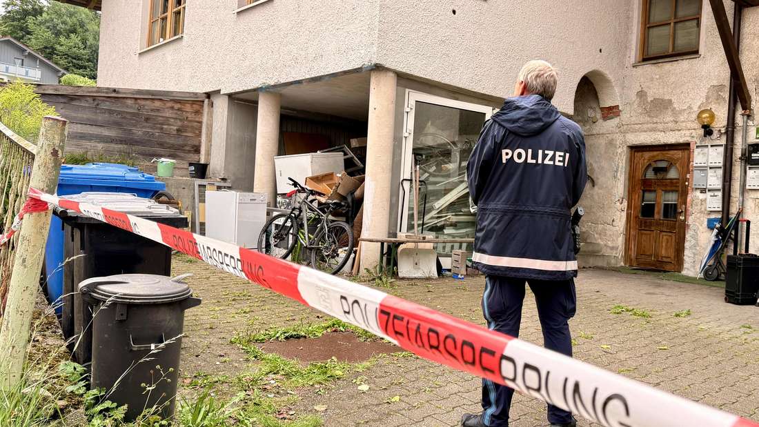 Ein Polizist steht hinter einer Absperrung vor einem Mehrfamilienhaus. In dem Haus im niederbayerischen Zwiesel sind drei Leichen gefunden worden.