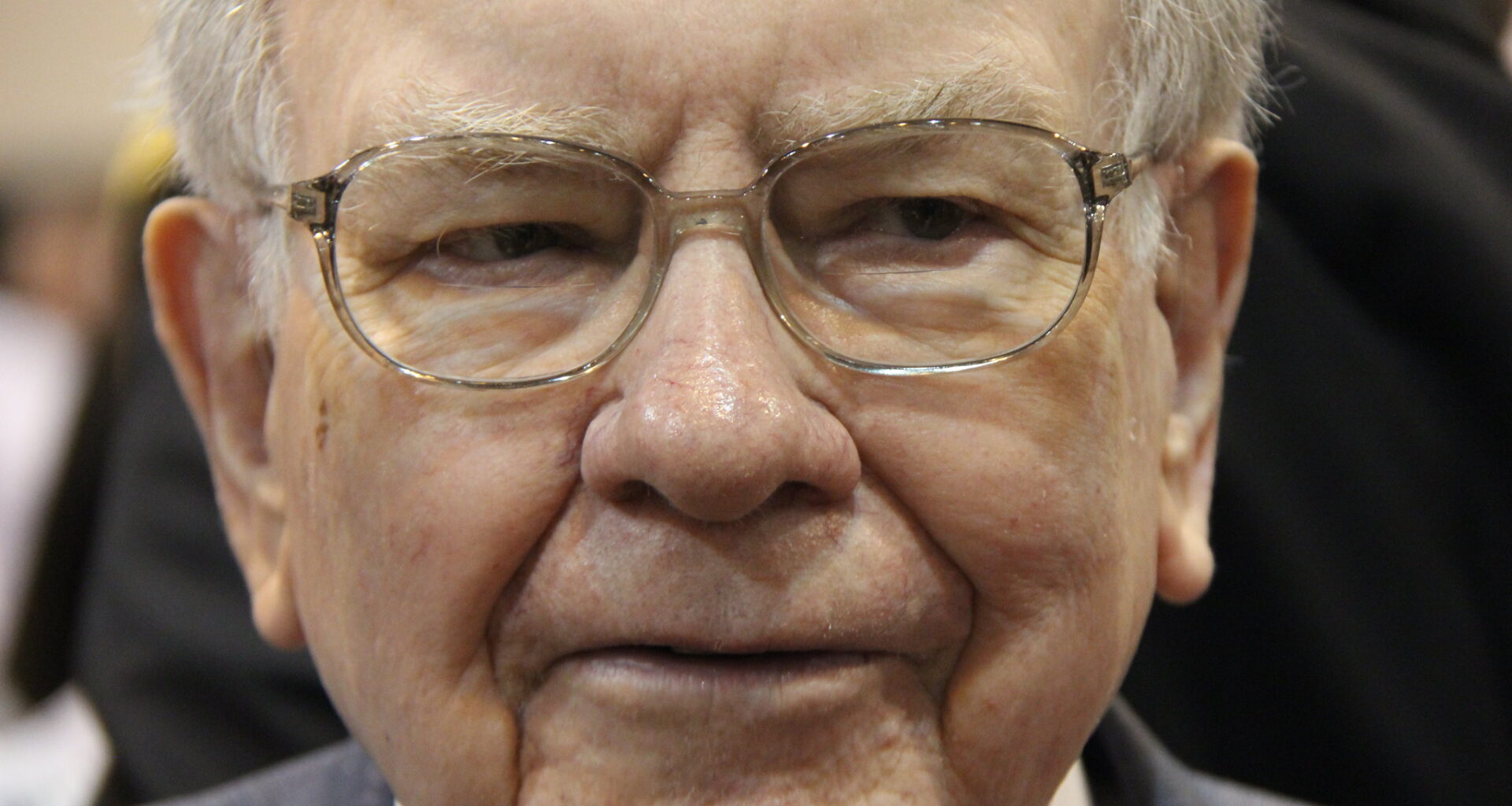 A pensive Warren Buffett surrounded by people at Berkshire Hathaway's annual shareholder meeting.