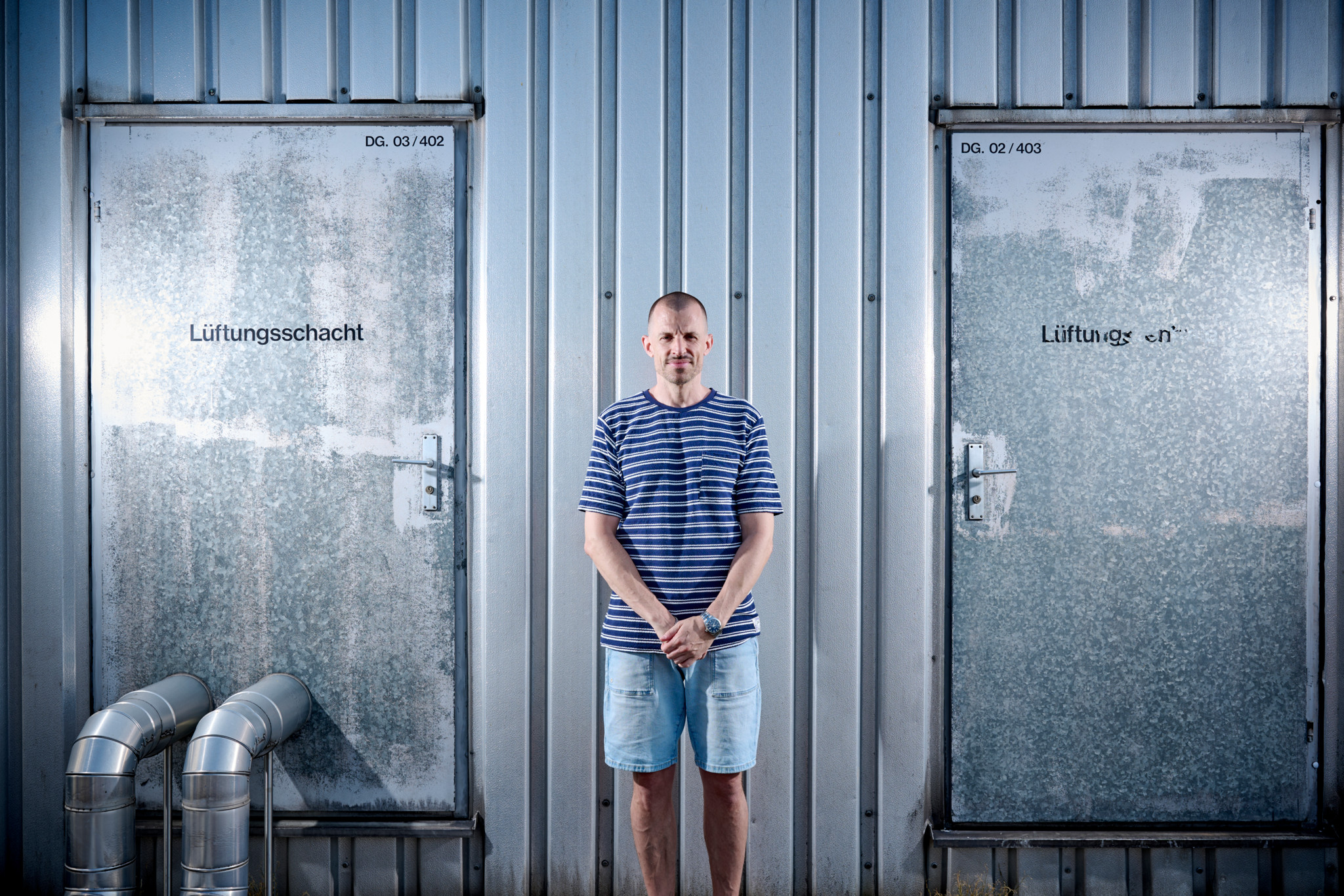 Simon Küffer alias Tommy Vercetti steht vor metallischen Lüftungsschächten, trägt ein gestreiftes T-Shirt und Jeansshorts. Simon Küffer alias Tommy Vercetti steht vor metallischen Lüftungsschächten, trägt ein gestreiftes T-Shirt und Jeansshorts.