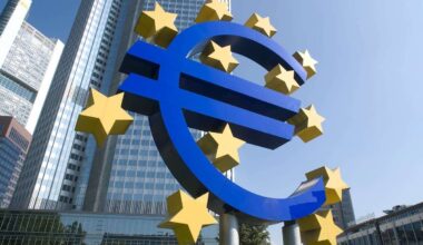 A large installation of the euro symbol in blue, surrounded by yellow stars, in front of a tall office building