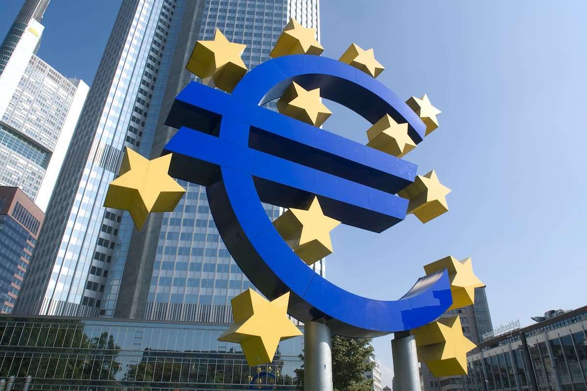A large installation of the euro symbol in blue, surrounded by yellow stars, in front of a tall office building