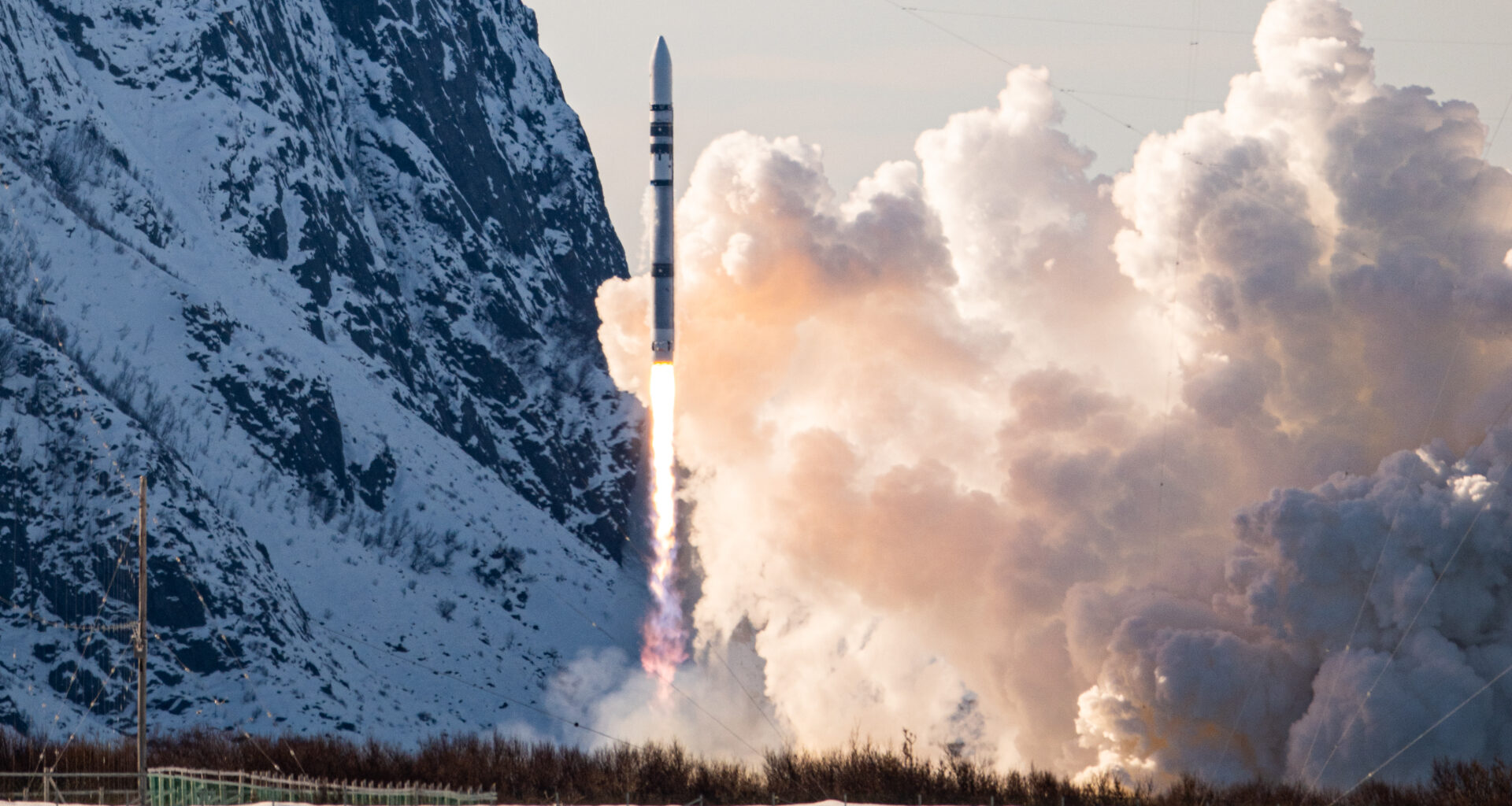 A white cylindrical rocket blasts off against a snowy landscape