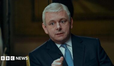 Michael Sheen in a blue suit and tie, and white shirt, as Prince Andrew in A Very Royal Scandal, being interviewed by the actor playing Emily Maitlis