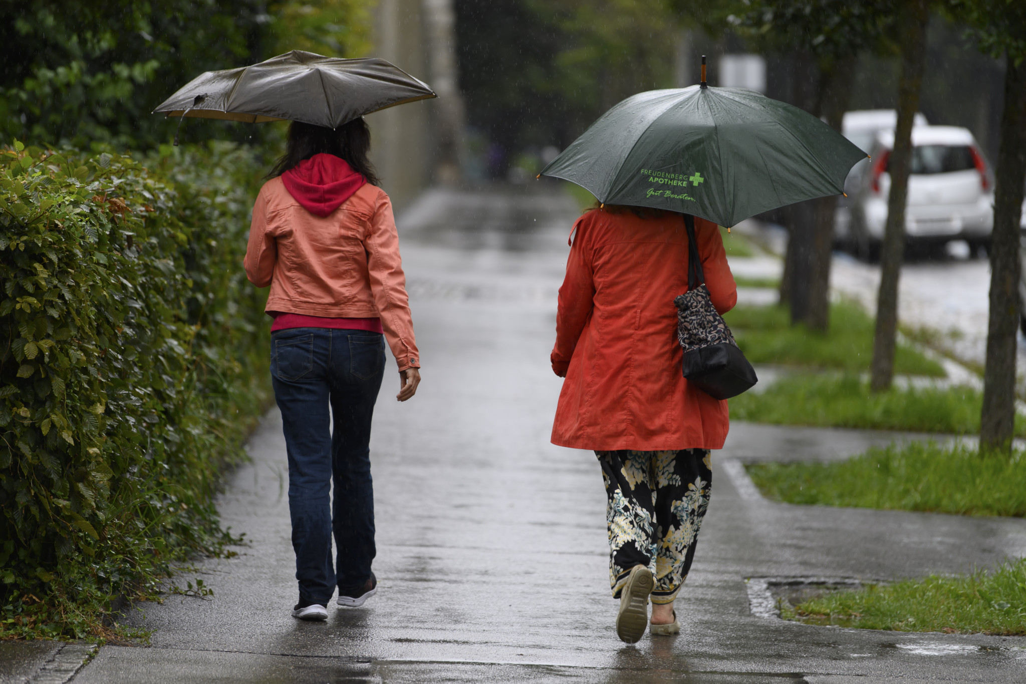 Zwei Personen mit Regenschirmen gehen bei Regenwetter auf einem Gehweg in Bern. Zwei Personen mit Regenschirmen gehen bei Regenwetter auf einem Gehweg in Bern.