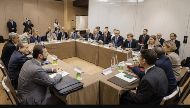 A meeting room where a group of diplomats and officials gather around a large table, engaging in discussions regarding nuclear talks between Iran and European countries.