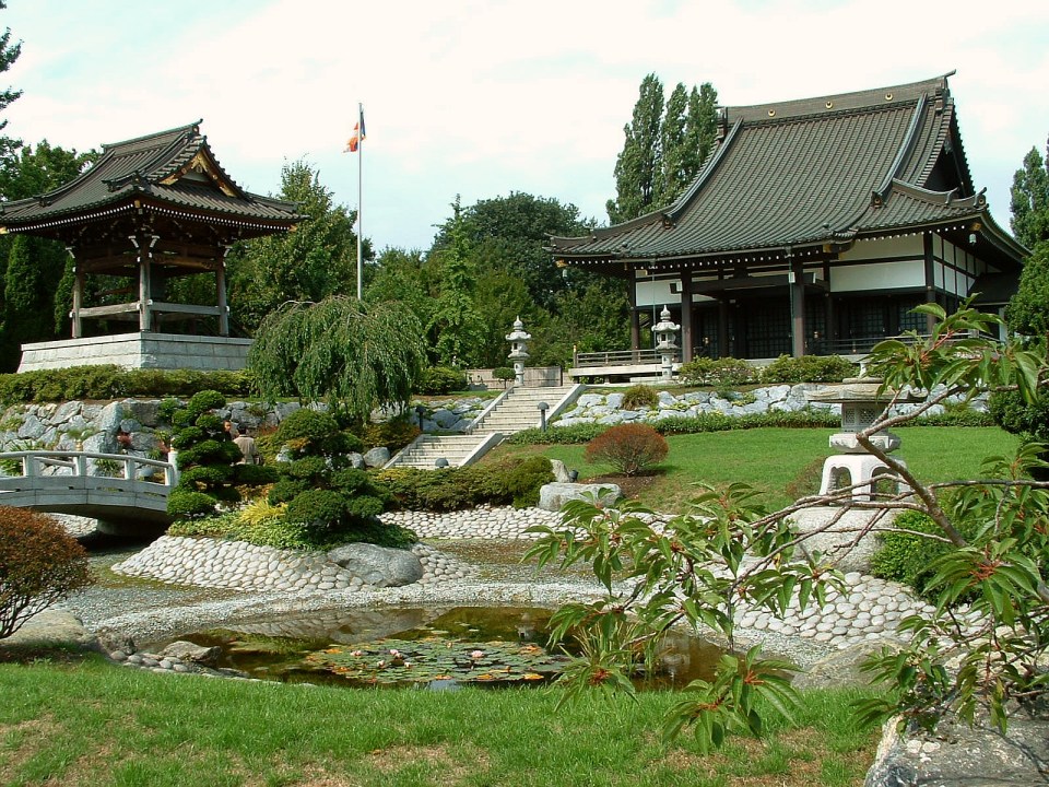 Japanese garden with two buildings, a pond, and a bridge.