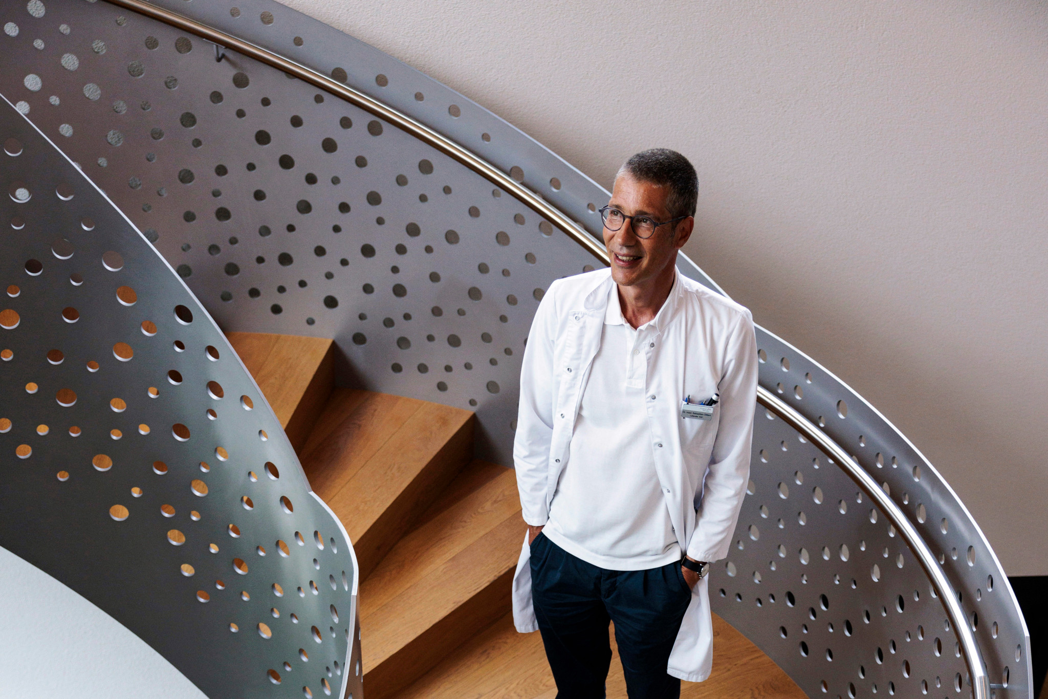 Dr. med. Sebastian Dittert steht lächelnd in einem modernen Treppenhaus der Privatklinik Meiringen. Dr. med. Sebastian Dittert steht lächelnd in einem modernen Treppenhaus der Privatklinik Meiringen.