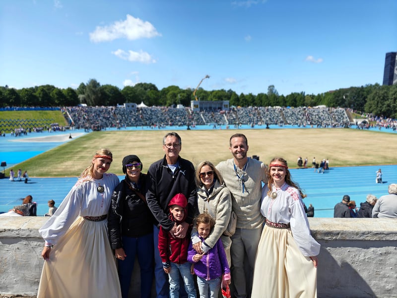 Lance McGavin, second from the right, with his parents, Myra and Scott McGavin; wife, Hailey; and kids Jett and Avery pause for a photo with folk dancers during the Estonian Dance Festival in Tallinn, Estonia, July 4, 2025.