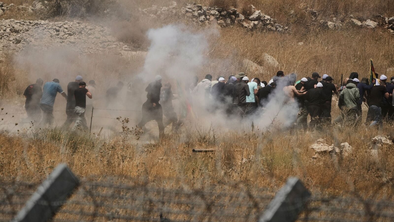 Syrian Druze run away from tear gas fired by Israeli soldiers as they protest on the Syrian side of the border with Israel, seen from Majdal Shams in the Israeli-controlled Golan Heights, Wednesday, July 16, 2025, amid the ongoing clashes between Syrian government forces and Druze armed groups in the southern Syrian city of Sweida. (AP Photo/Leo Correa)