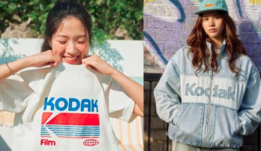 Two young women wear Kodak-branded clothing; one smiles while pulling up a white Kodak T-shirt, and the other stands against a wall in a light denim Kodak jacket and cap.