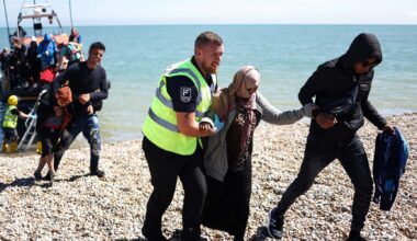 An interforce officer helps a woman on the beach at Dungeness on the southeast coast of England after she disembarked from a Royal National Lifeboat Institution (RNLI) lifeboat after being picked up at sea with other migrants while attempting to cross the English Channel from France on August 16, 2023. (Henry Nicholls/AFP via Getty Images)