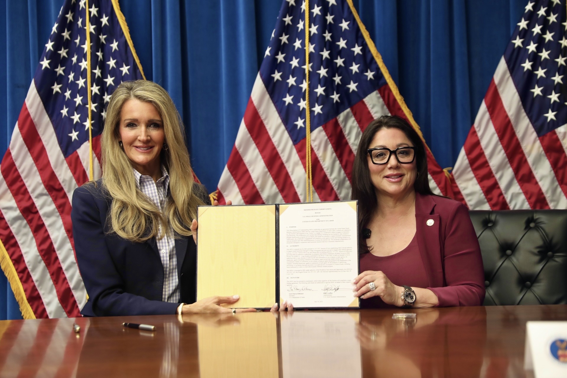 A woman in a blue blazer and a woman in maroon hold a signed document.
