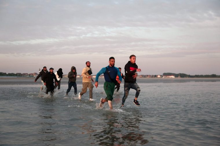 A group of migrants run from the beach into the water to reach an inflatable dinghy to leave the coast of northern France in an attempt to cross the English Channel to reach Britain as tougher migration controls were announced, at the beach of Petit-Fort-Philippe in Gravelines, near Calais, France, July 17, 2025. REUTERS/Gonzalo Fuentes