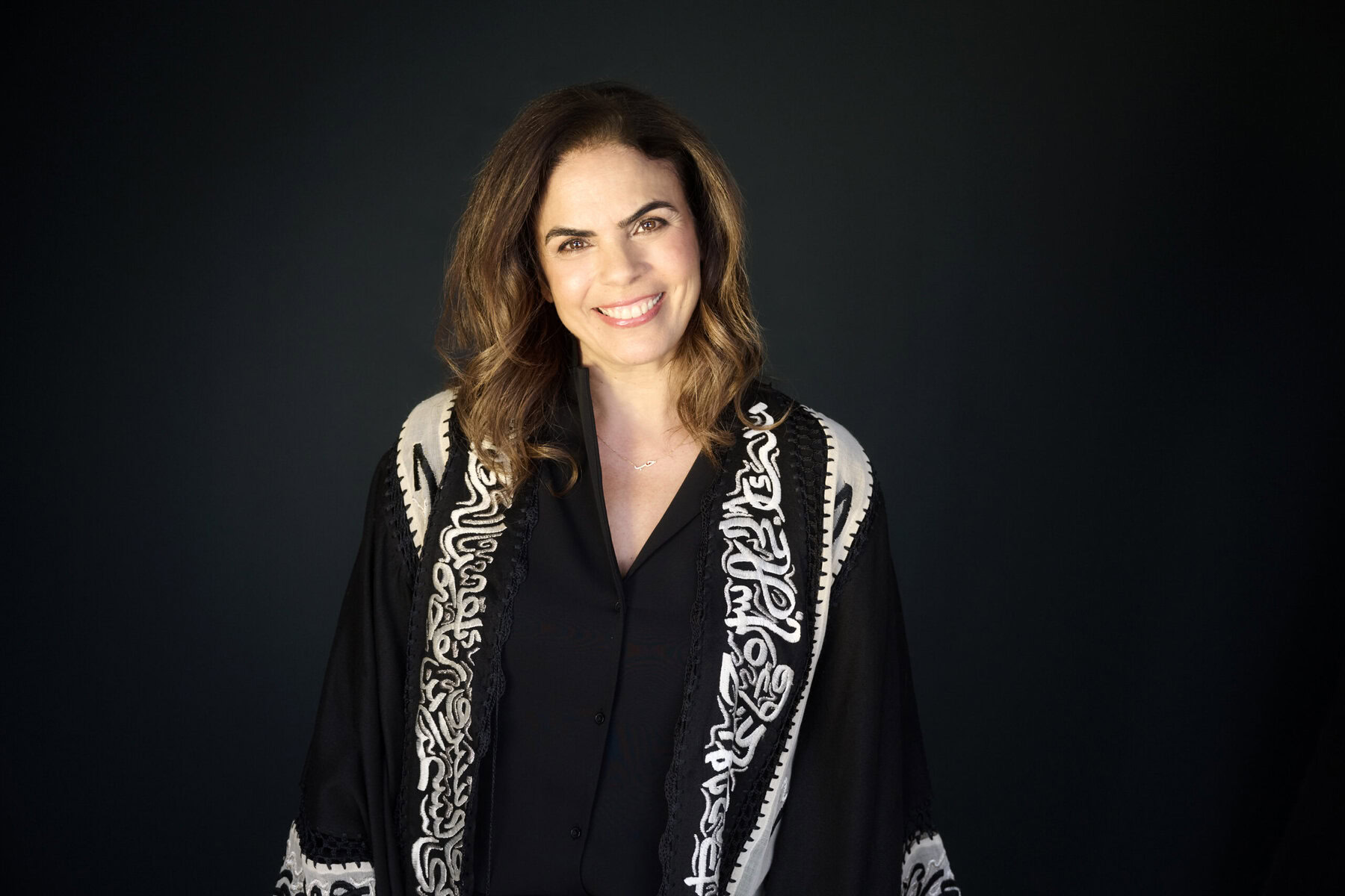 Headshot of Shireen Abu Khader. She is dressed in black and white and standing in front of a black background.