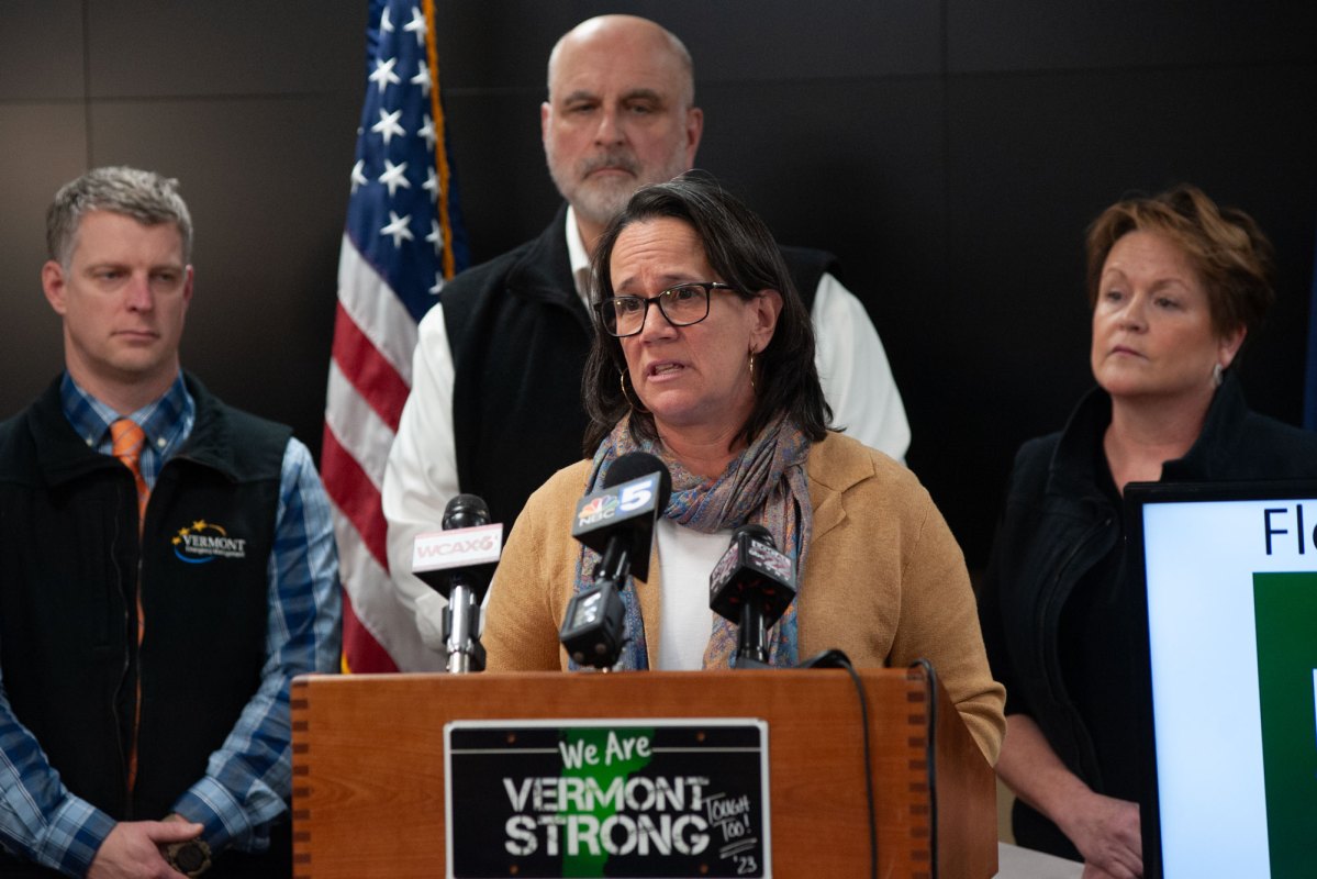 A woman speaks at a podium with three people in the background.