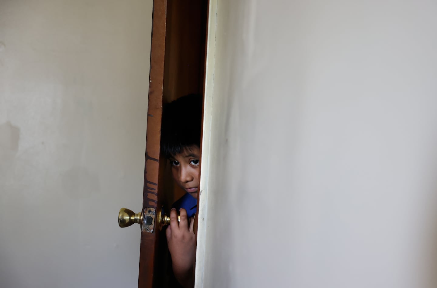 Ery Perez Gutierrez, 9, peered through the door into the living room of his family’s apartment in Springfield on July 15. Ery participated in a summer program last year but since President Trump froze education funds for the Migration Education Program, a grant that supports children of agricultural and fishery workers, he has had to stay home instead.