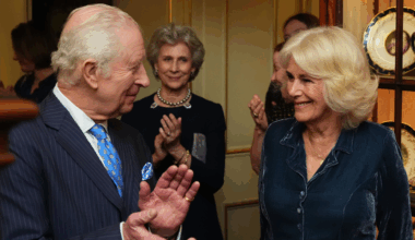 King Charles clapping and smiling at Queen Camilla, who is dressed in a blue dress