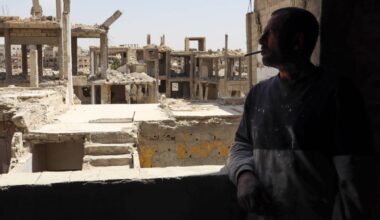 Hassan Tamim, 52, looks out the window of his apartment at the skeletons of neighboring buildings in the Yarmouk Palestinian refugee camp in Damascus, 30/4/2025 (Natacha Danon)