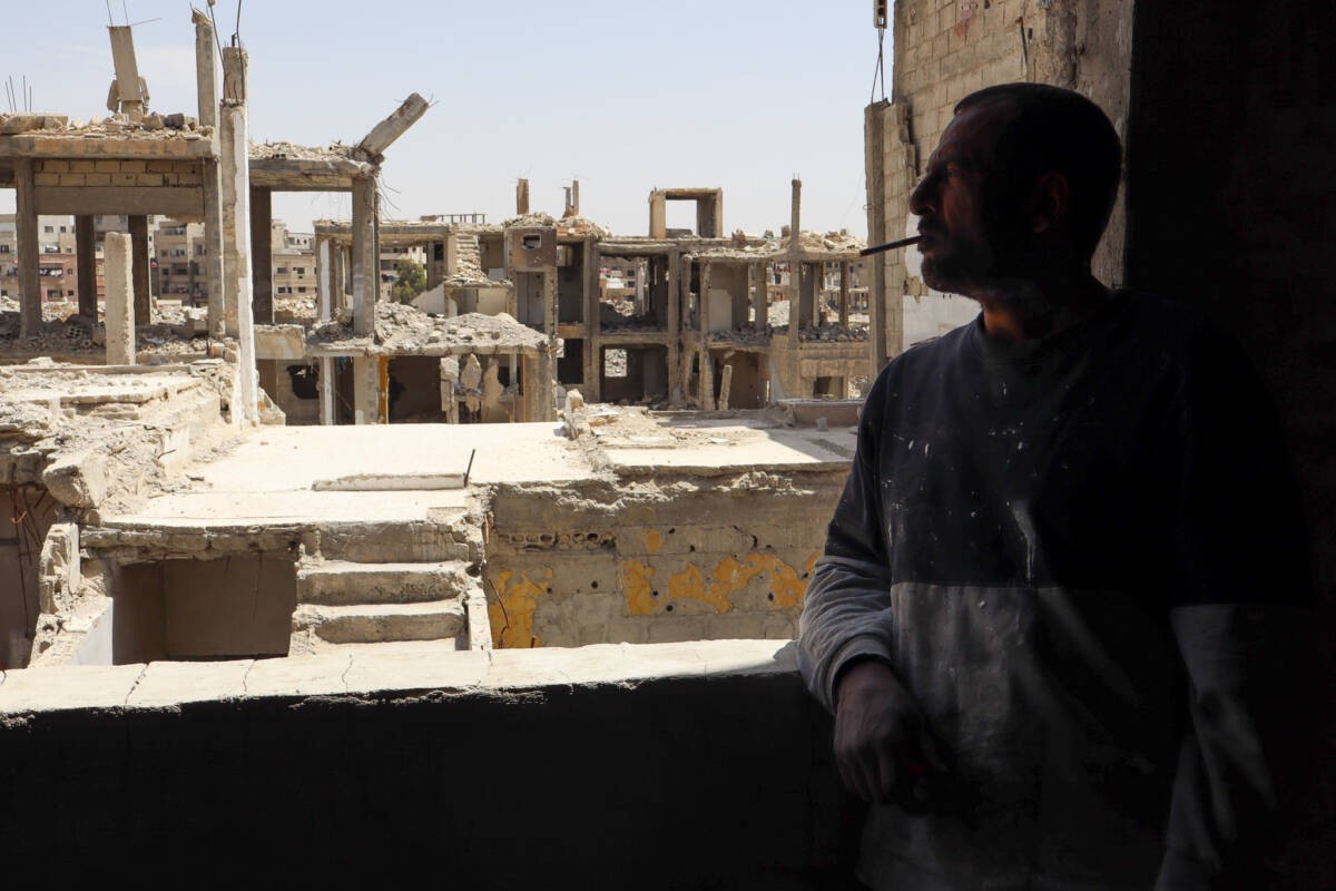 Hassan Tamim, 52, looks out the window of his apartment at the skeletons of neighboring buildings in the Yarmouk Palestinian refugee camp in Damascus, 30/4/2025 (Natacha Danon)