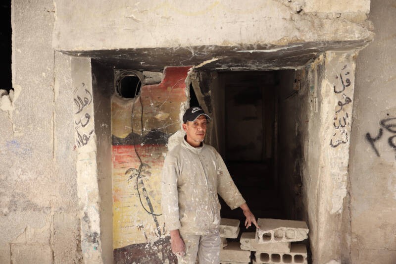Amin Saeed Hafez, 52, stands at the entrance of his home in Yarmouk camp’s Magharebeh neighborhood. Before installing a door, he blocked the entrance with cinderblocks to keep stray dogs out of the building, 30/4/2025 (Natacha Danon/Syria Direct)