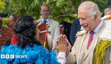 King Charles III greets an Indigenous leader - an Earth Elder - wearing a headdress and a dazzling robe of blue feathers.