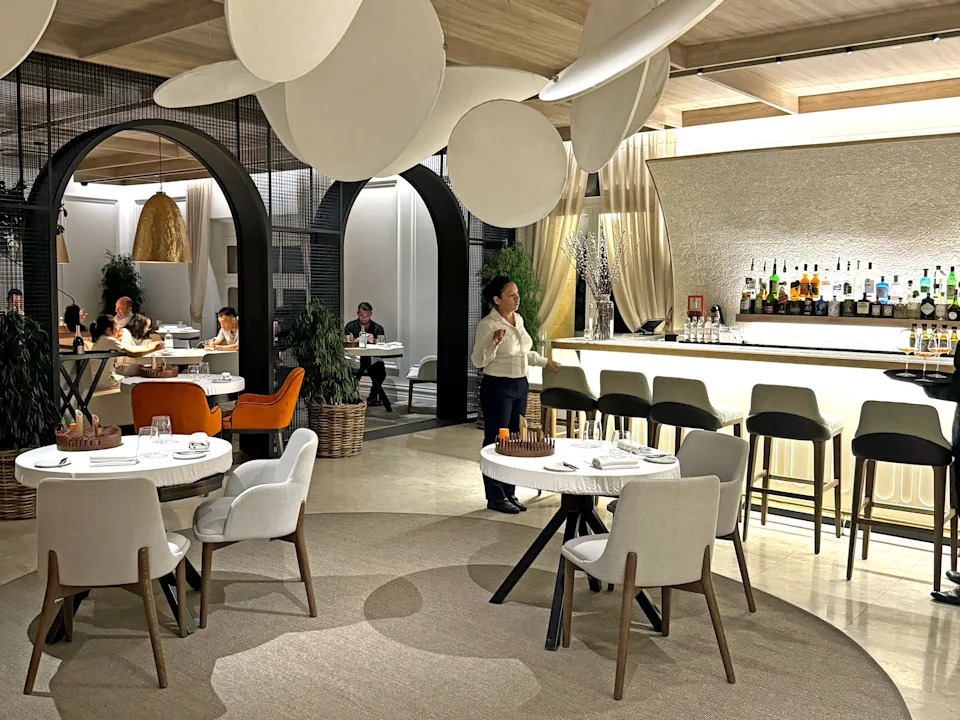 A server walks through a chic restaurant with round tables and a bar.