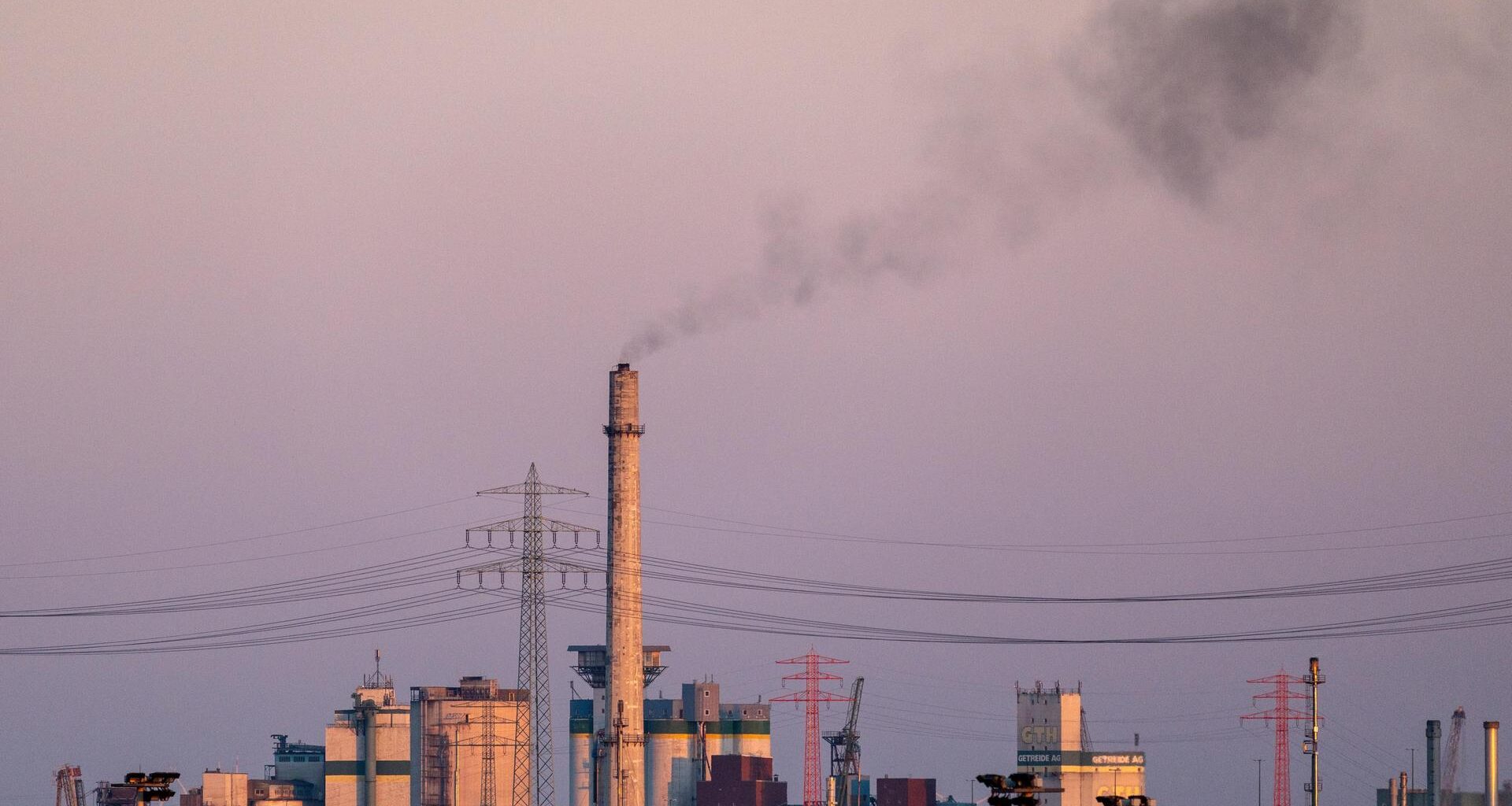 Ein hoher Industrieschornstein stößt bei Dämmerung dunkle Rauchwolken aus.