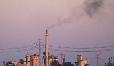 Ein hoher Industrieschornstein stößt bei Dämmerung dunkle Rauchwolken aus.
