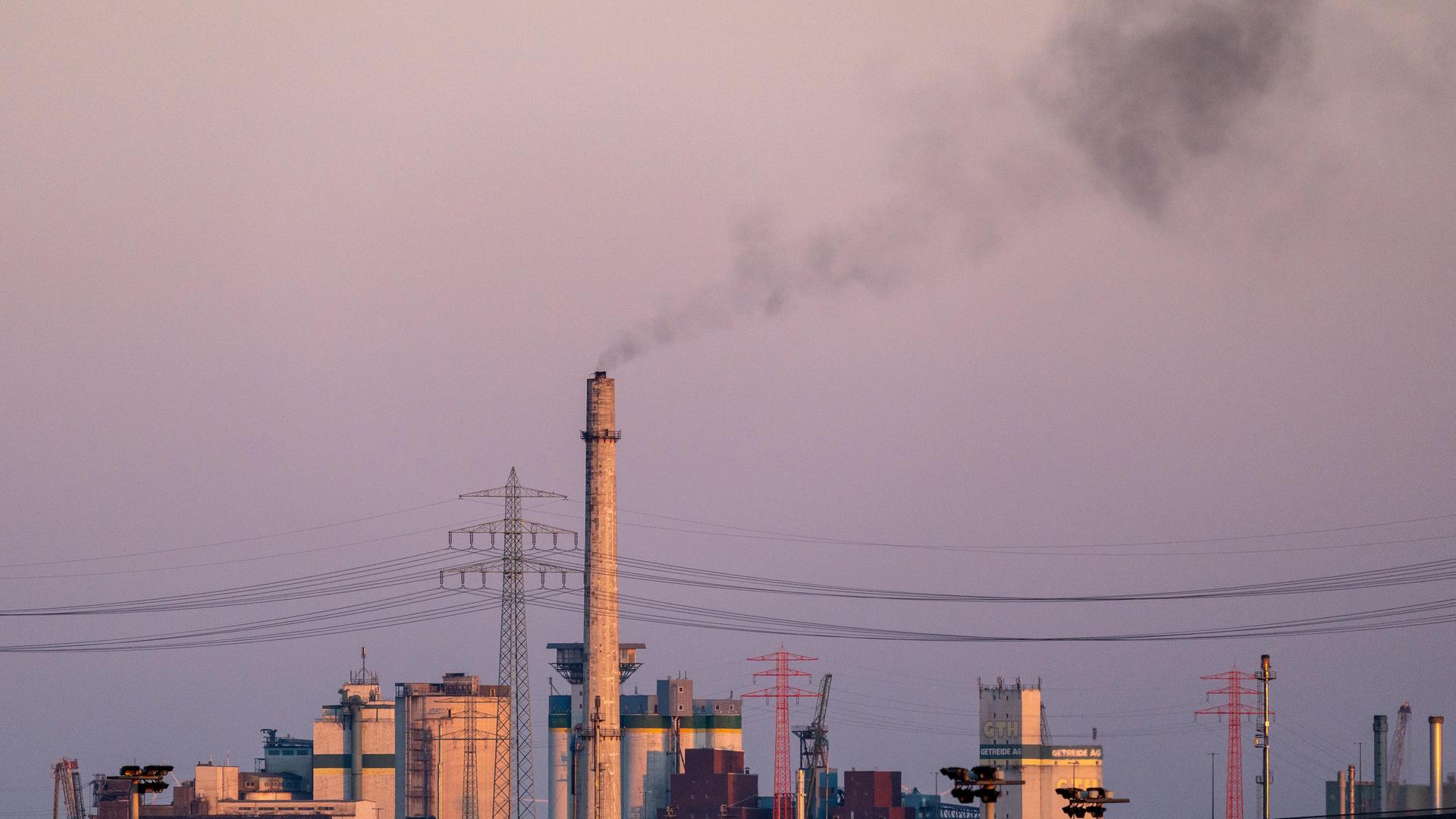 Ein hoher Industrieschornstein stößt bei Dämmerung dunkle Rauchwolken aus. Ein hoher Industrieschornstein stößt bei Dämmerung dunkle Rauchwolken aus.