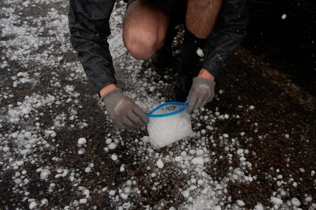 Tony Illenden crouches outside Northern Illinois University's Husky Hail Hunter to scoop hail into a bag while in a hailstorm during a Project ICECHIP operation, June 6, 2025, in Levelland, Texas. (Carolyn Kaster/AP)