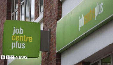 Green, white and yellow sign attached to a brick building with "job centre plus" written on it.
