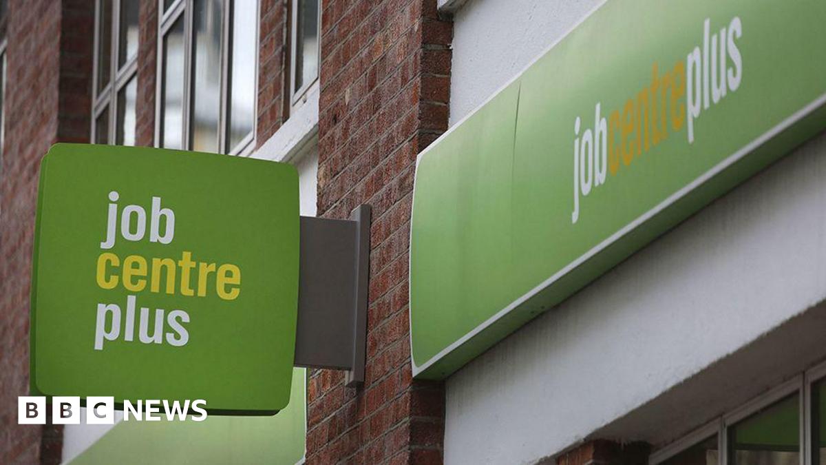 Green, white and yellow sign attached to a brick building with "job centre plus" written on it.