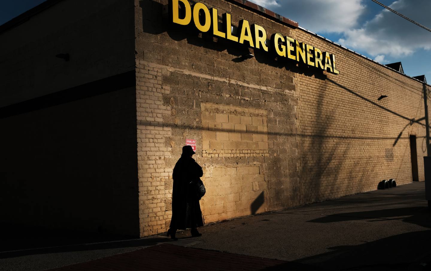 A woman in a dark coat walks by a Dollar General store in New York City