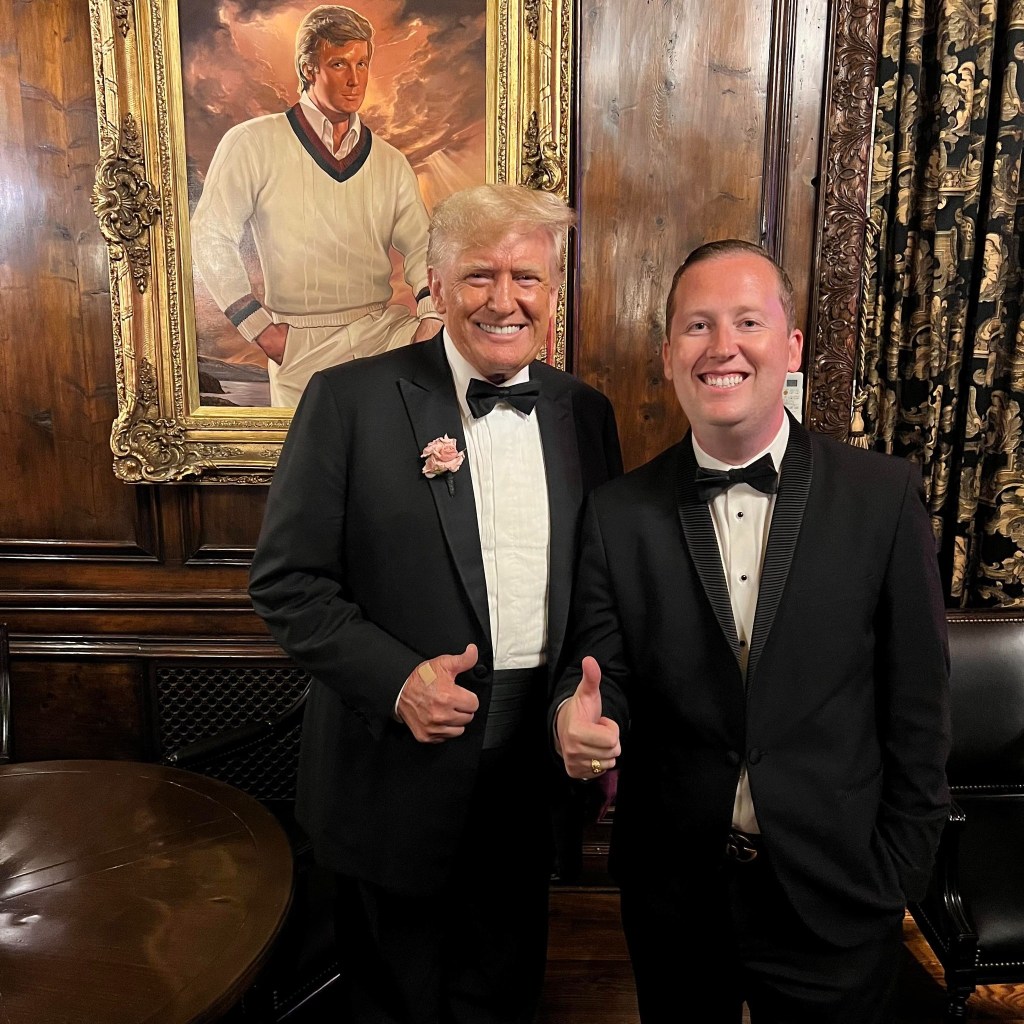 Donald Trump and another man in tuxedos giving thumbs up.  A framed portrait is in the background.