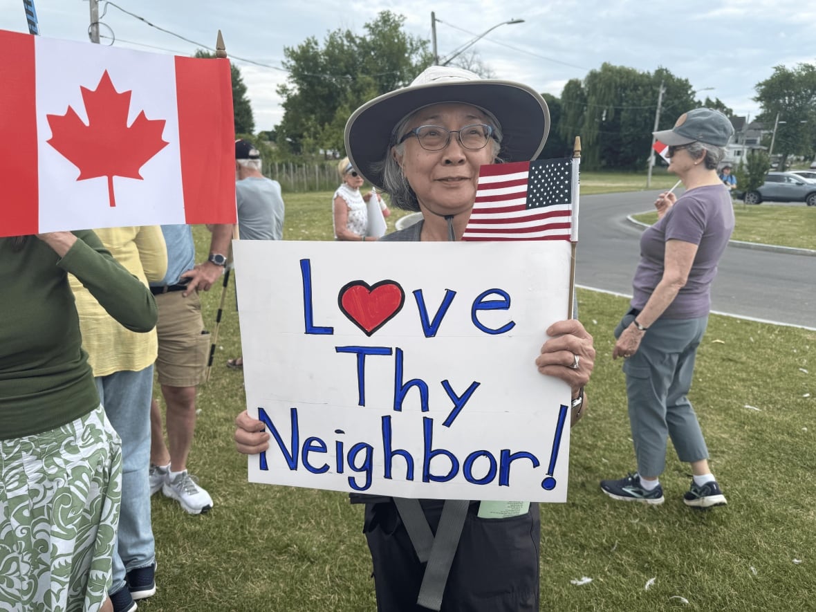A woman holds sign that says "Love Thy Neighbour"