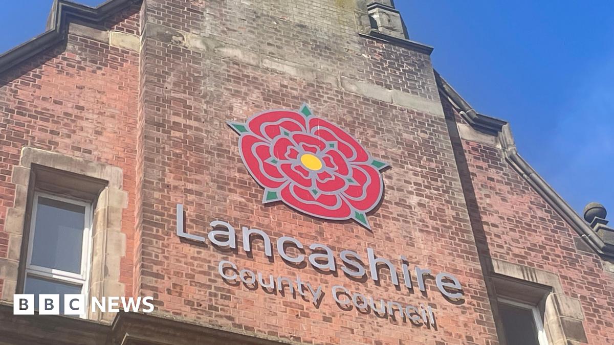 Lancashire County Council sign, with the red rose emblem, on the side of a tall, redbrick building. The photograph was taken on a sunny day with clear blue skies.