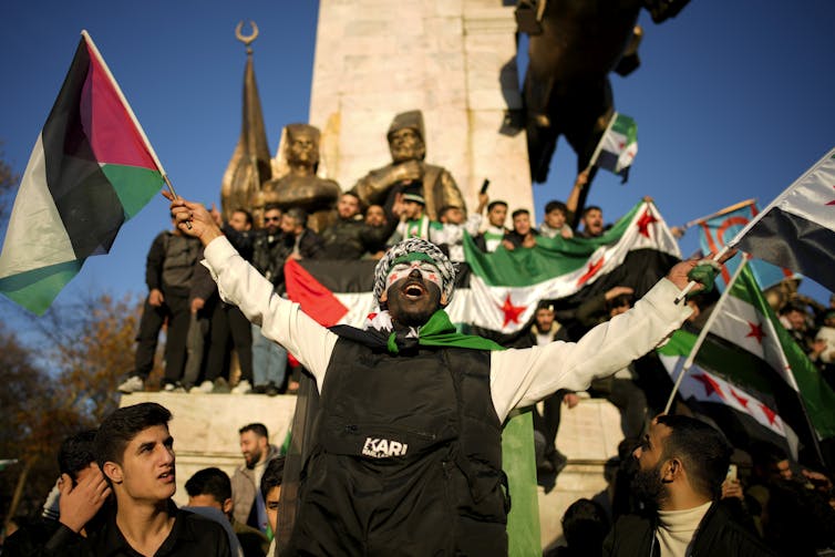 A man with a painted face and waving a Syrian flag celebrates.