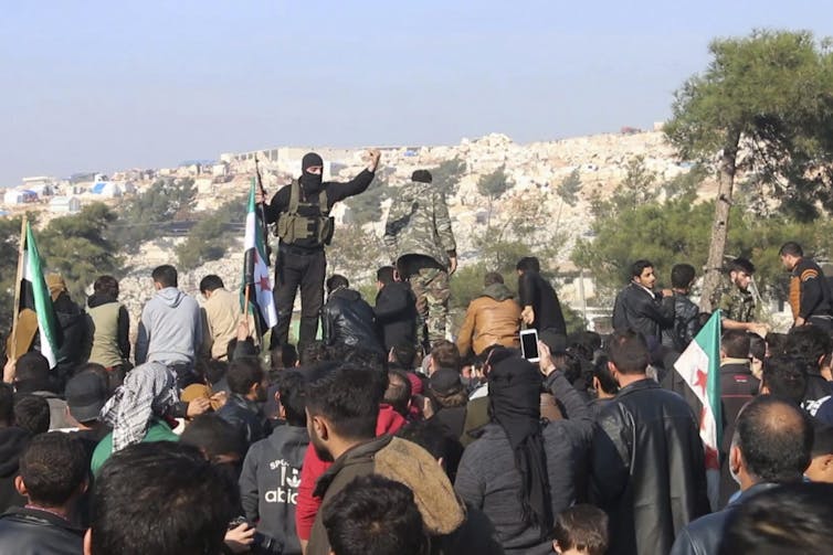 An armed man raises his hand in front of a group of protesters.