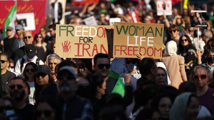 a crowd of people, two signs are held up in the crowd - one reads 'free Iran' the other 'woman, life, freedom'