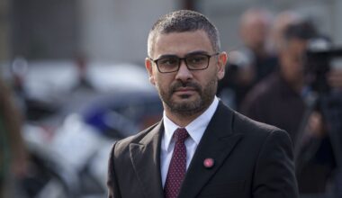 Florin Manole poartă un sacou negru, o cămașă albă și o cravată roșie cu buline negre. Poartă și ochelari, care au rame negre